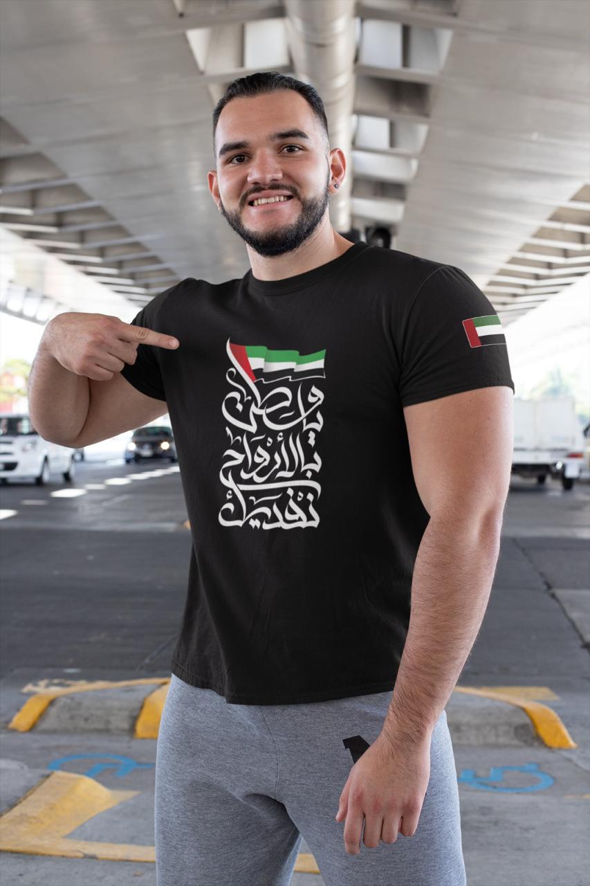 WhatsAppImage2020-11-24at7.53.58PM_1_75f46fbc-2e1f-4d65-ba74-2d8101e33871 | UAE SPORT STORE Smiling man in a black T‑shirt with Arabic typography, pointing to the print under a highway overpass.