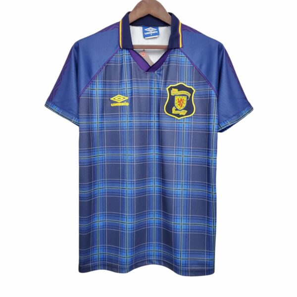 Blue plaid football jersey with a yellow-bordered crest on the left chest reading 'The Scottish Football Association' and a yellow Umbro logo on the right chest, hanging on a wooden hanger.