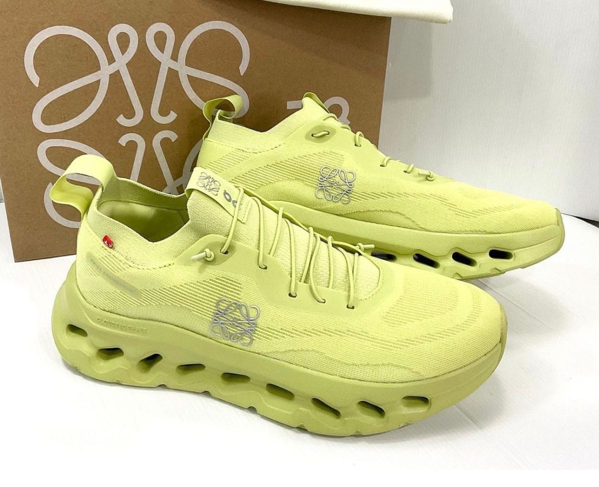 Lime-yellow athletic sneakers with a chunky hollow-sole design, knits upper, and logo on the side, placed before a brown box.