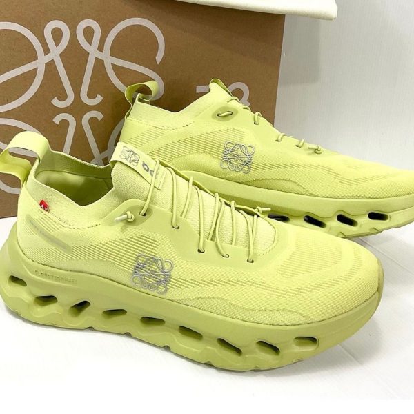 Lime-yellow athletic sneakers with a chunky hollow-sole design, knits upper, and logo on the side, placed before a brown box.
