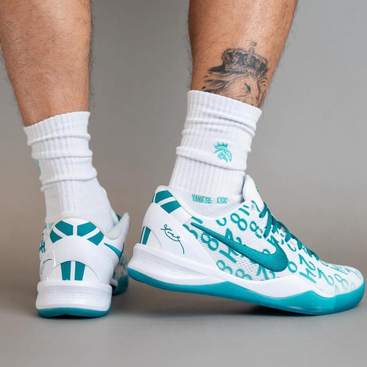 Low-angle shot of white and teal running shoes on a person wearing white socks, showing teal accents and graphic print on the sides.