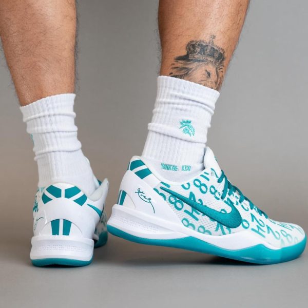 Low-angle shot of white and teal running shoes on a person wearing white socks, showing teal accents and graphic print on the sides.