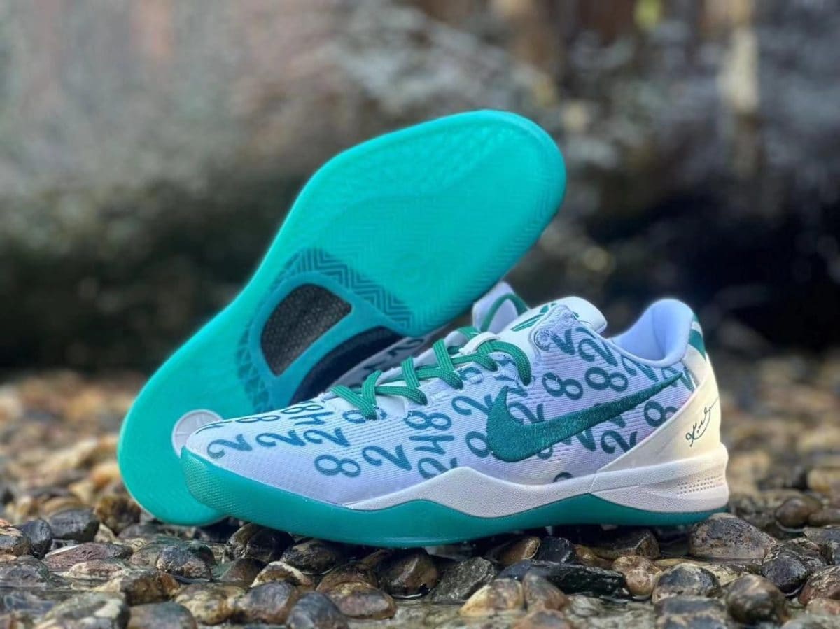 White running shoes with turquoise accents and a numeric pattern on the upper, placed on a rocky outdoor surface.