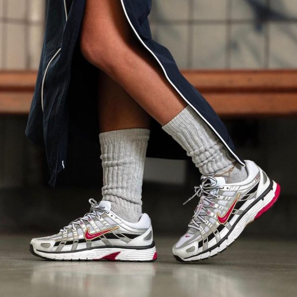 Person wearing gray knee-high socks and silver-white Nike running shoes with pink swooshes, standing on a polished floor in a navy outfit.