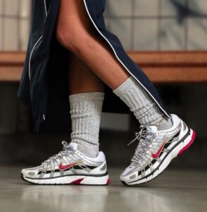 Close-up of silver and white Nike running shoes with pink swoosh, gray socks, and a dark jacket.