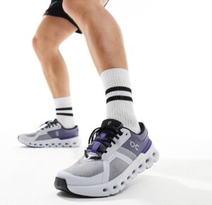 Athlete wearing gray and purple On Cloud running shoes with white socks mid-stride, focus on footwear design.