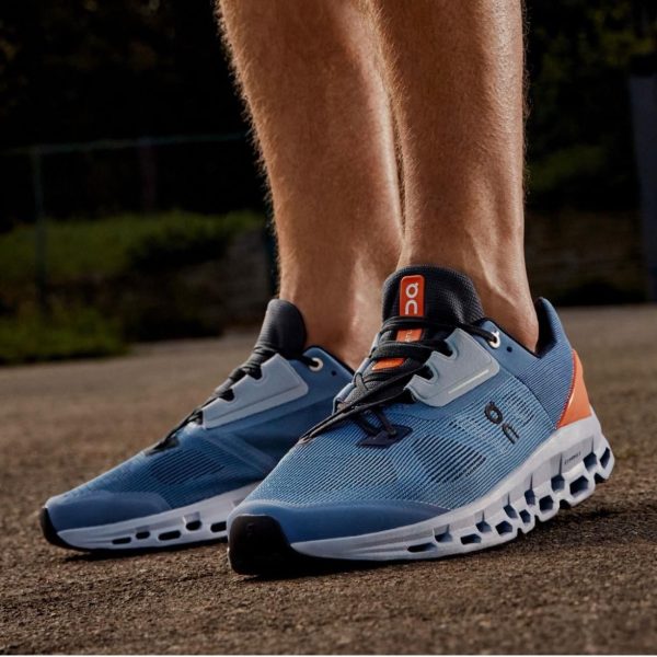Close-up of blue On running shoes with a distinctive segmented sole on a paved path outdoors, laces tied.