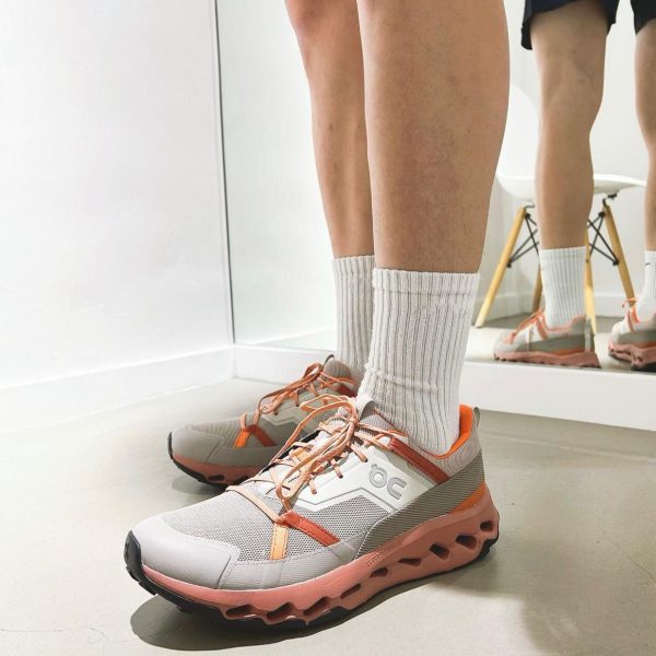 Person wearing peach and gray running shoes with white socks, standing in a bright room with a mirror behind them.