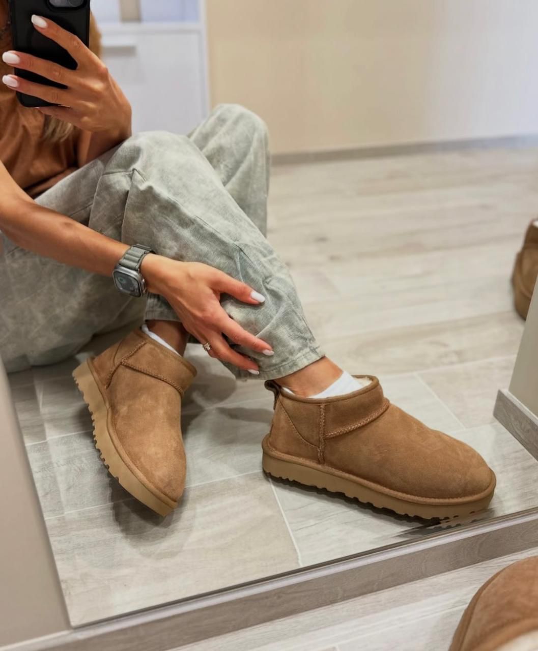 WhatsAppImage2025-01-11at10.19.50 | UAE SPORT STORE Person sitting on the floor in a fitting room, taking a mirror selfie, wearing gray jeans, white socks, a tan suede ankle boot, and a silver smartwatch.
