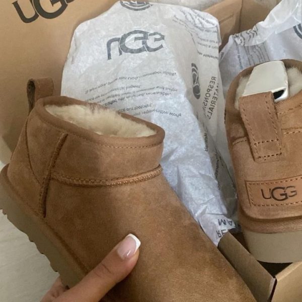 Tan suede UGG boots with shearling lining held in hand beside packaging labeled UGG and a 'fall season' sticker visible.