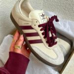 WhatsAppImage2025-01-12at09.46.32 | UAE SPORT STORE Cream Adidas Samba sneaker with burgundy stripes and laces being held in a hand over a box.