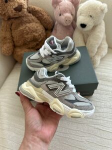 Gray and white New Balance chunky sneakers held in hand with a shoe box and three stuffed bears in the background.