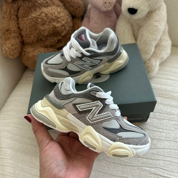Gray and white New Balance chunky sneakers held in hand with a shoe box and three stuffed bears in the background.