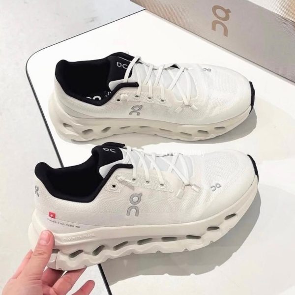 Pair of white On Running sneakers with black inner lining on a display table, logo visible on the side.