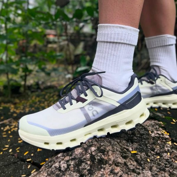 Person wearing light sneakers and white crew socks standing on a rocky surface outdoors, greenery in the background.