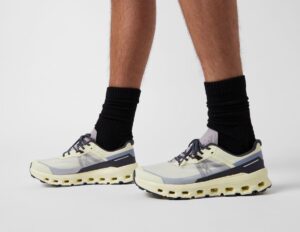 Pair of light gray and cream athletic sneakers with a chunky cream sole, worn with black crew socks, photographed from the side and front on a white background.