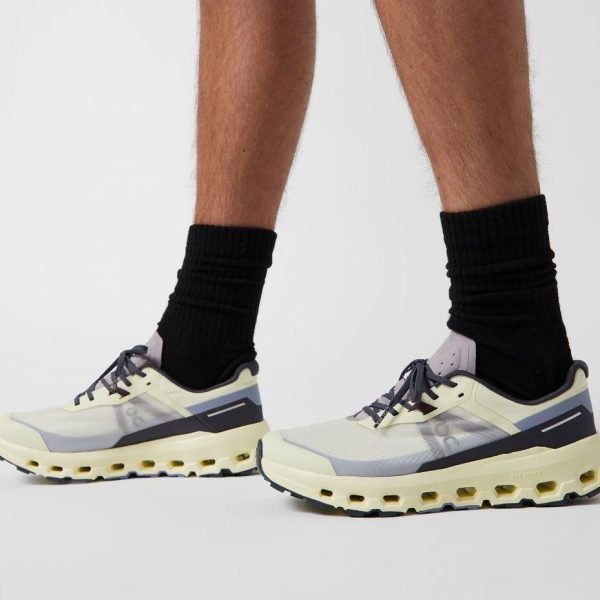 Pair of light gray and cream athletic sneakers with a chunky cream sole, worn with black crew socks, photographed from the side and front on a white background.