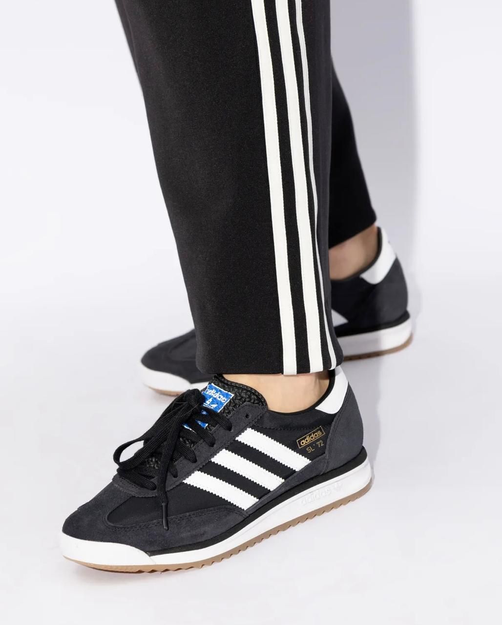 WhatsAppImage2025-04-15at11.26.53 | UAE SPORT STORE Black Adidas sneakers with white stripes and laces, worn with black track pants featuring white side stripes.