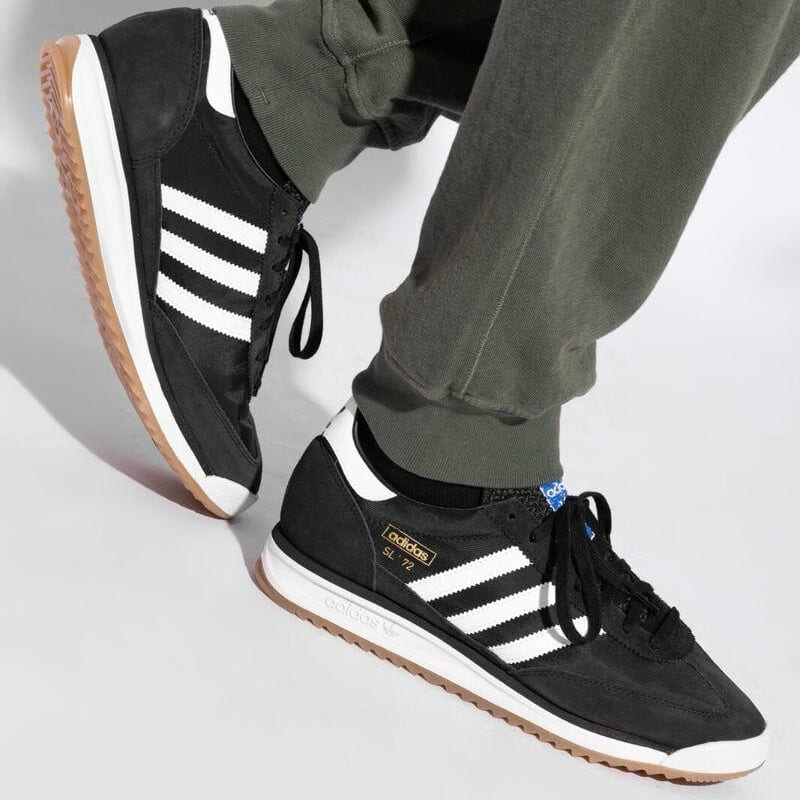 WhatsAppImage2025-04-15at11.27.03_2 | UAE SPORT STORE Black Adidas sneakers with white stripes and gum sole, being worn by a person wearing olive-green pants