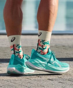 Close-up of turquoise running shoes and patterned white socks standing on pavement.