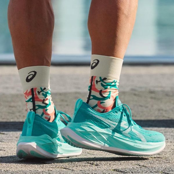 Close-up of turquoise running shoes and patterned white socks standing on pavement.