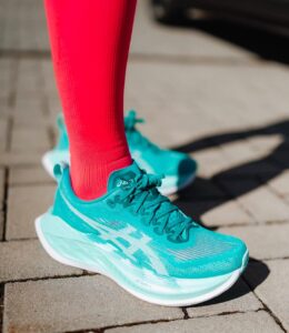 Turquoise running shoes with bright pink socks on a paved sidewalk surface.