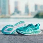 Turquoise running shoes resting on a textured pavement with a blurred city skyline in the background.