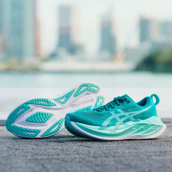 Turquoise running shoes resting on a textured pavement with a blurred city skyline in the background.