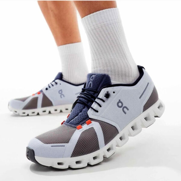 Pair of modern running shoes in white, gray, and navy with a chunky segmented sole, worn with white socks.