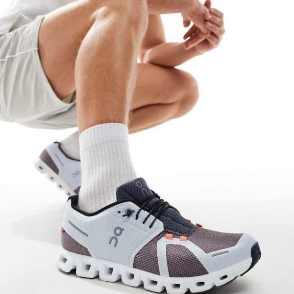 Close-up of a blue-gray running shoe with a distinctive white chunked sole on a person crouching or kneeling, showing white socks and shorts.
