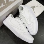 Pair of all-white Nike Air sneakers (Air Force 1) with a matching box on a dark surface; front shoes show perforated toe and clean laces.