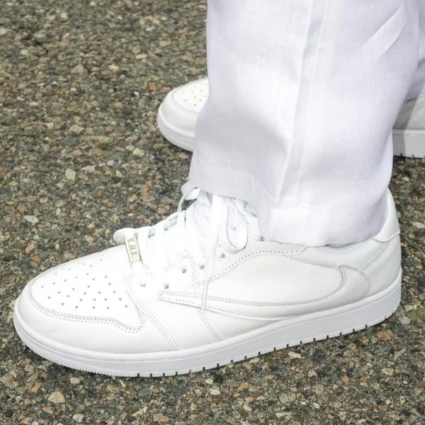 All-white sneakers with laces on a rough pavement, worn with white pants (side view).