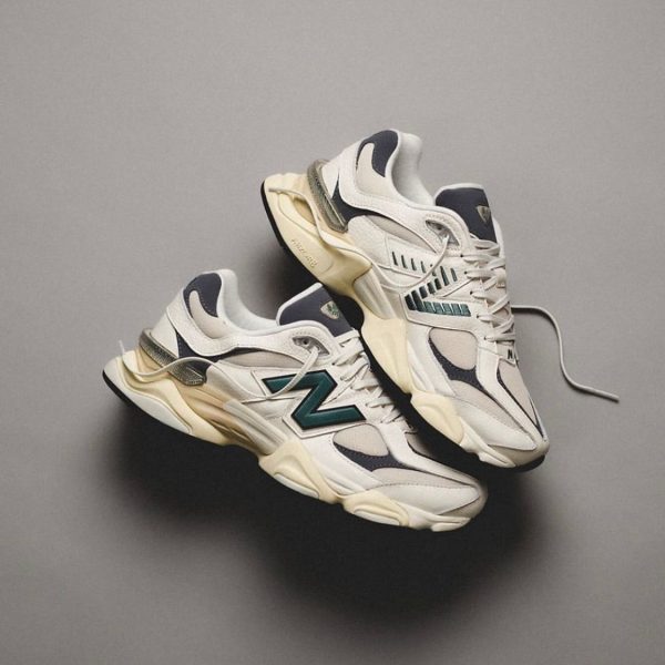 Pair of white New Balance sneakers with teal NB logo lying on a gray surface, laces loose.