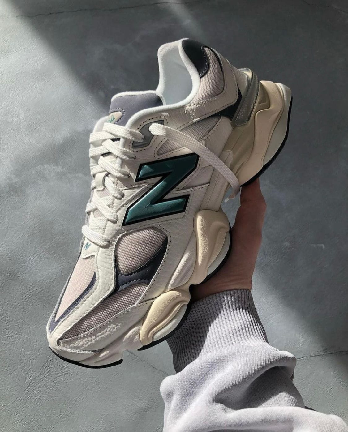 WhatsApp_Image_2024-07-27_at_00.39.11 | UAE SPORT STORE White athletic sneaker with teal New Balance 'N' logo held in a hand against a gray floor.