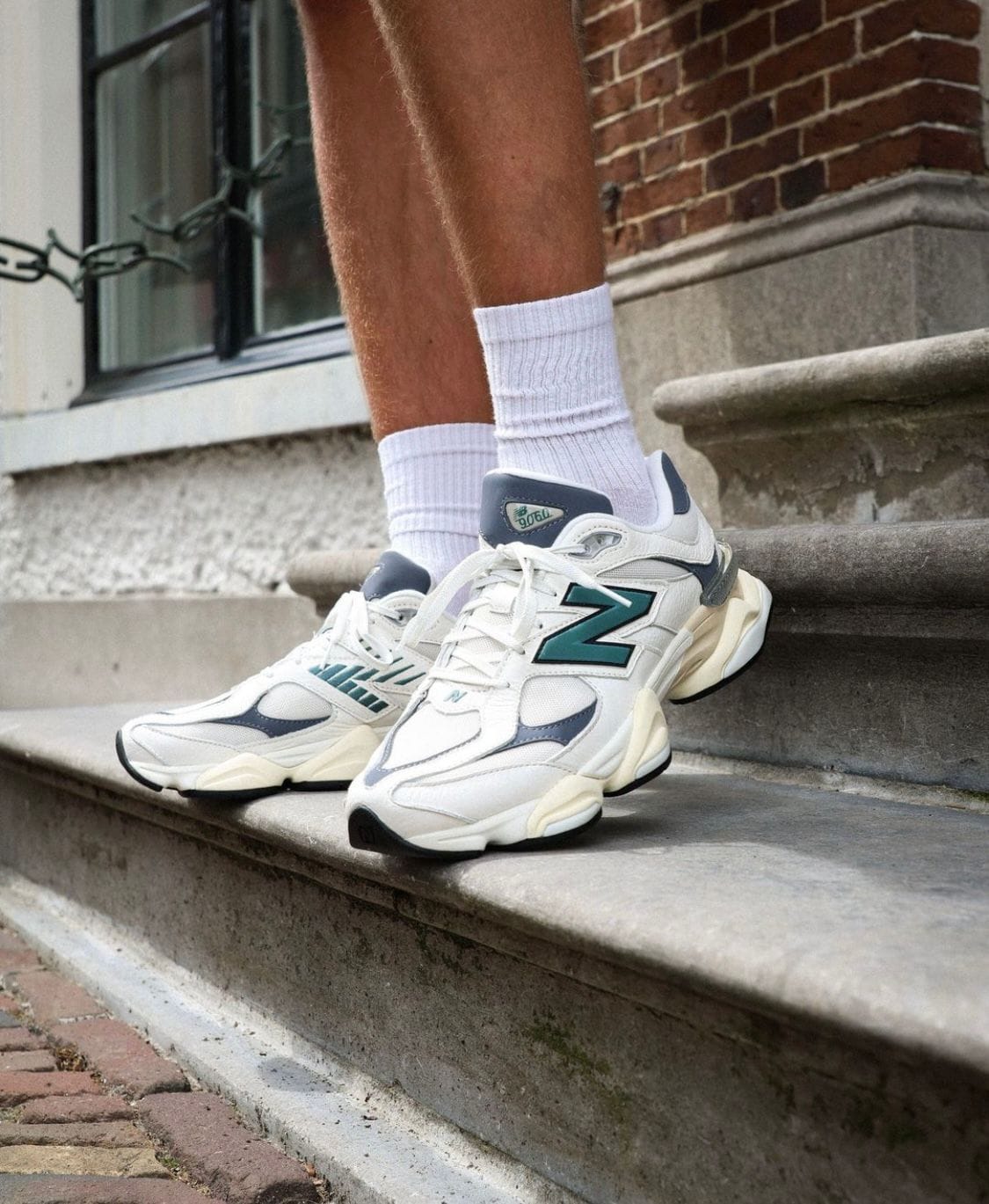 WhatsApp_Image_2024-07-27_at_00.39.18 | UAE SPORT STORE White and teal New Balance sneakers on a person standing on outdoor stone steps, wearing white crew socks (focus on footwear).