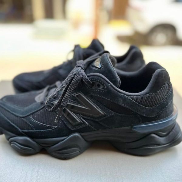 Black chunky-soled sneakers on a table outdoors, laces tied, with a blurred background.