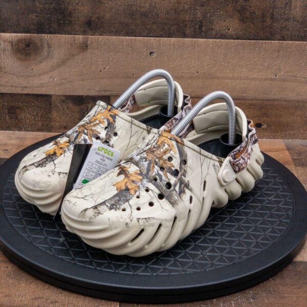 WhatsApp_Image_2024-09-06_at_09.18.55 | UAE SPORT STORE Pair of beige camouflage Crocs with ventilation holes, displayed on a black circular platform, tags attached to the shoe.