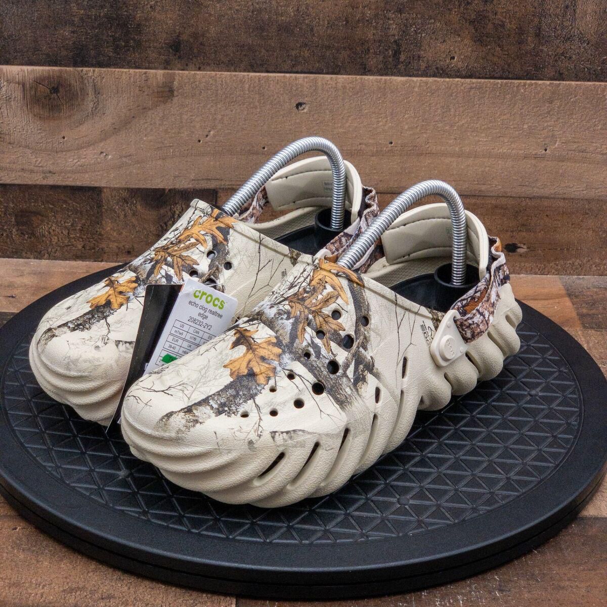 WhatsApp_Image_2024-09-06_at_09.18.55 | UAE SPORT STORE Pair of beige camouflage Crocs with ventilation holes, displayed on a black circular platform, tags attached to the shoe.