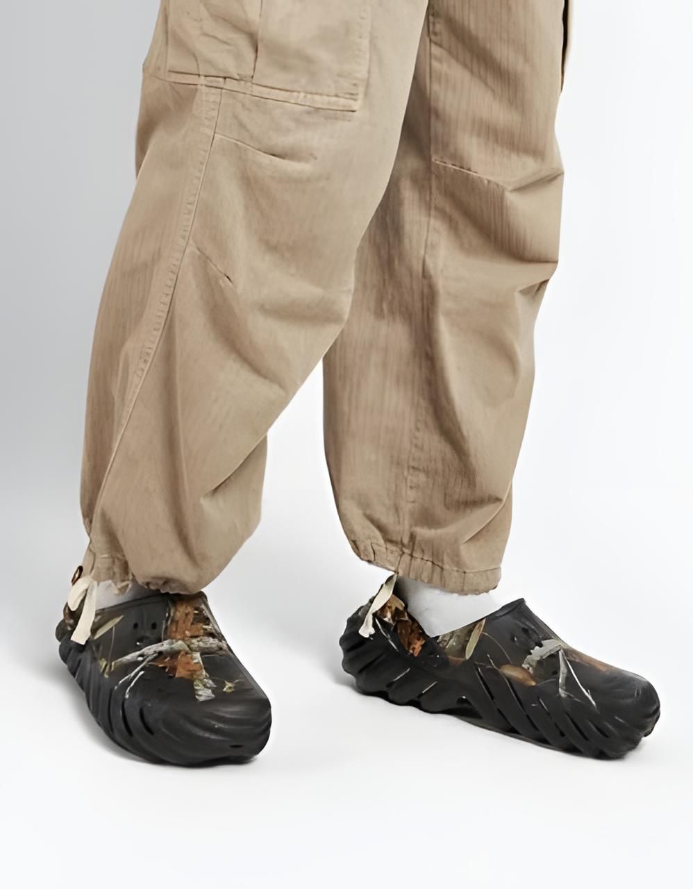 WhatsApp_Image_2024-09-06_at_11.31.56 | UAE SPORT STORE Lower body of a person in tan cargo pants wearing damaged black protective shoe covers with torn edges and white laces on a white studio floor.