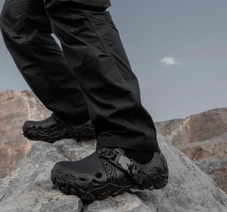 WhatsApp_Image_2024-09-07_at_09.58.06 | UAE SPORT STORE Black hiking shoes with a rugged lug sole stepping on a rocky surface amid a canyon landscape.