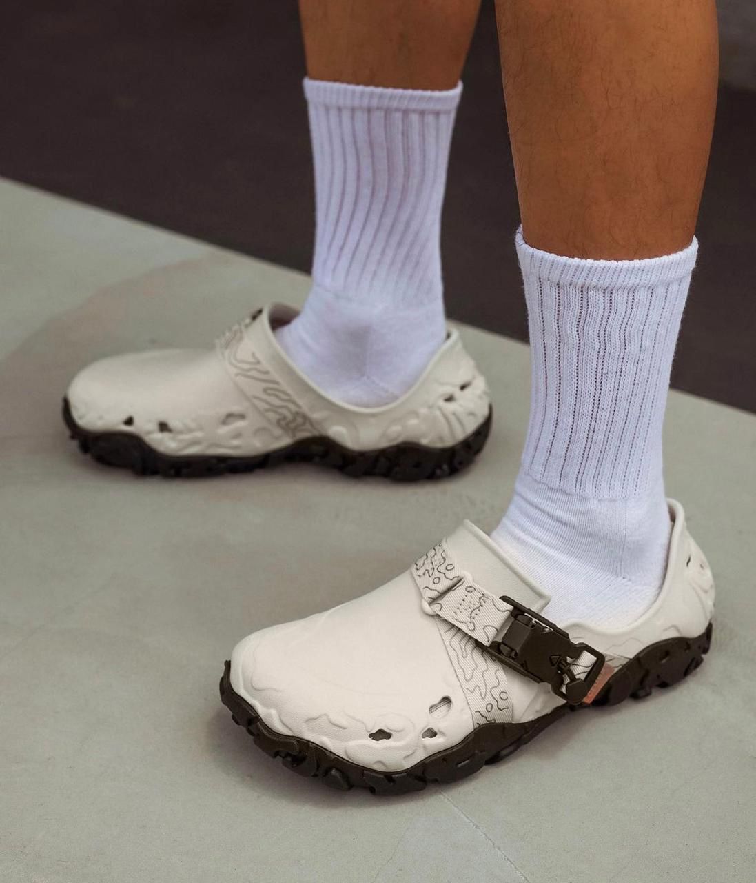 WhatsApp_Image_2024-09-07_at_11.22.30 | UAE SPORT STORE Person wearing white open-toe sandals with a black rugged sole and white crew socks on a light floor edge of a room.