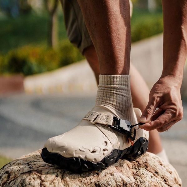 WhatsApp_Image_2024-09-07_at_11.22.32 | UAE SPORT STORE Close-up of a person tying the strap on a beige hiking boot while standing on a rock.