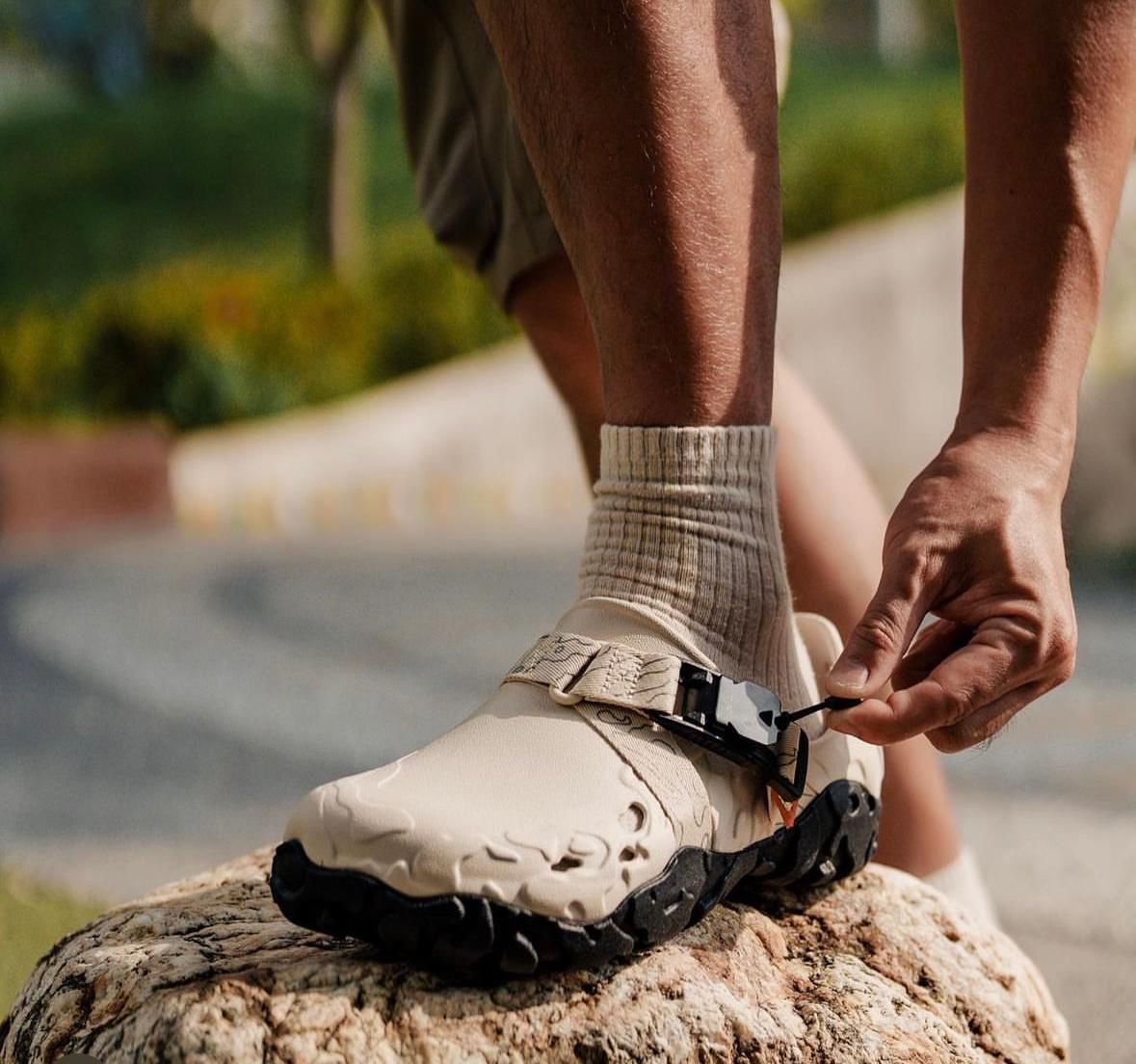 WhatsApp_Image_2024-09-07_at_11.22.32 | UAE SPORT STORE Close-up of a person tying the strap on a beige hiking boot while standing on a rock.