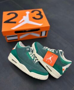 Pair of green sneakers with white soles and an orange Air Jordan tag, placed on a dark surface with an orange Jordan box in the background.