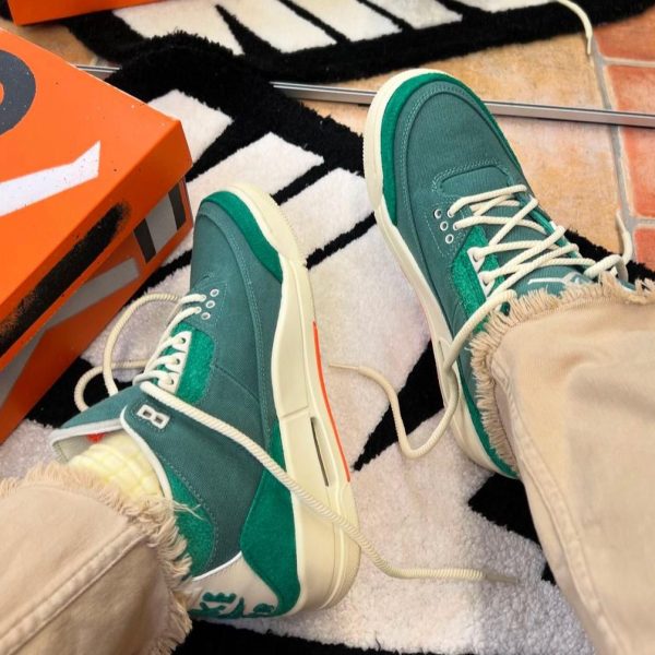 Teal sneakers with white laces and thick cream soles resting on a patterned rug next to an orange shoebox.
