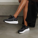 WhatsApp_Image_2024-09-08_at_12.13.03 | UAE SPORT STORE Woman wearing black sneakers with a chunky white sole, resting one foot on a step.