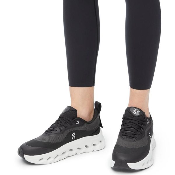 Black and gray athletic running shoes with a thick white sole, worn by a person in black leggings on a white background.