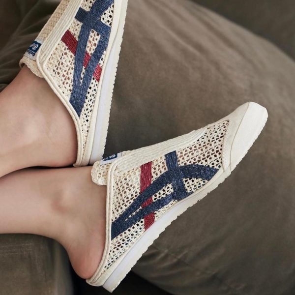 Cream woven slip-on sneakers with blue and red stripes resting on a sofa, showing the side and sole.