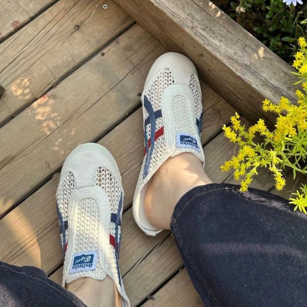 Beige mesh slip-on sneakers on a wooden deck next to yellow flowering plants, viewed from above.