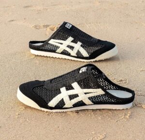 WhatsApp_Image_2024-10-03_at_15.09.57 | UAE SPORT STORE Black mesh slip-on shoes with white crisscross stripes on sandy beach surface.
